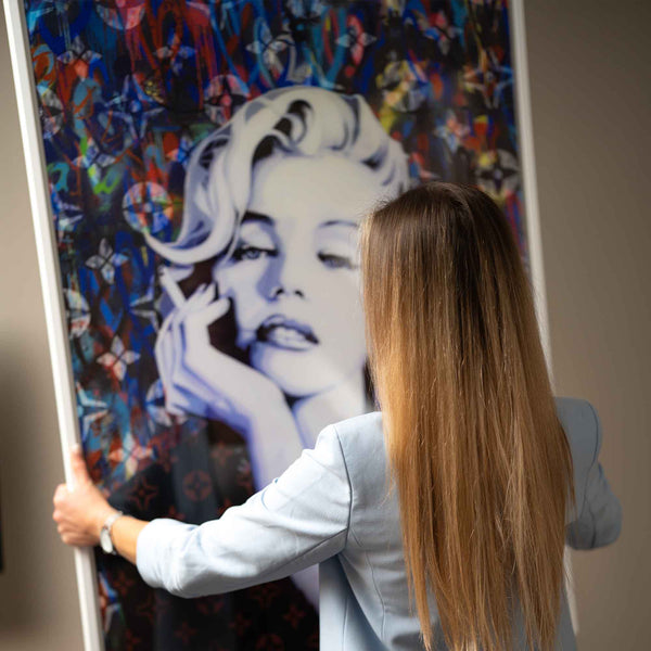 Frau hängt modernes Pop Art Wandbild mit Porträt einer Frau vor buntem Hintergrund auf.
